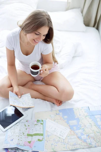Giovane donna rilassata seduta sul letto con una tazza di caffè e tablet digitale — Foto Stock