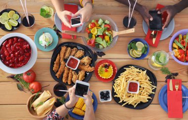 Ahşap masada otururken birlikte yemek yiyen bir grup insanın üst düzey görüntüsü. Masada yemek var. İnsanlar fast food yiyor..