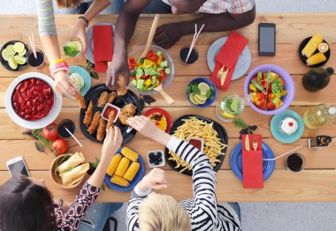 Ahşap masada otururken birlikte yemek yiyen bir grup insanın üst düzey görüntüsü. Masada yemek var. İnsanlar fast food yiyor..
