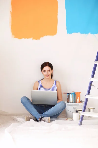 Junges Frauenporträt beim Bemalen der neuen Wohnung, sitzend mit Laptop — Stockfoto