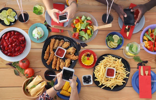 Ahşap masada otururken birlikte yemek yiyen bir grup insanın üst düzey görüntüsü. Masada yemek var. İnsanlar fast food yiyor..