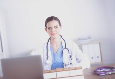 Güzel, genç, gülümseyen bayan doktor masada oturuyor ve yazıyor.