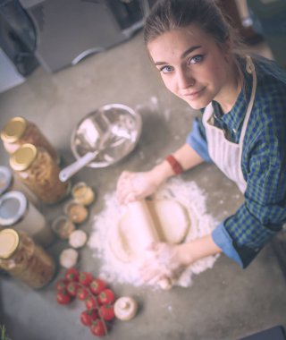 Güzel bir kadın mutfakta pasta pişiriyor. Masanın yanında duruyor..