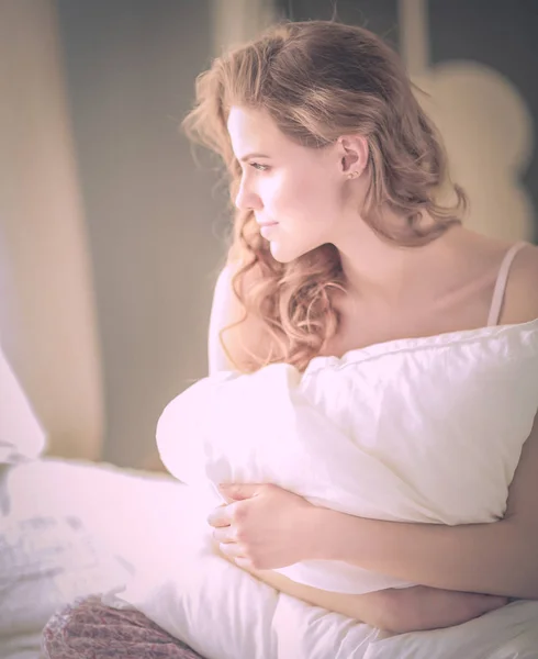 Ung kvinna med en kudde medan du sitter på sin säng. — Stockfoto