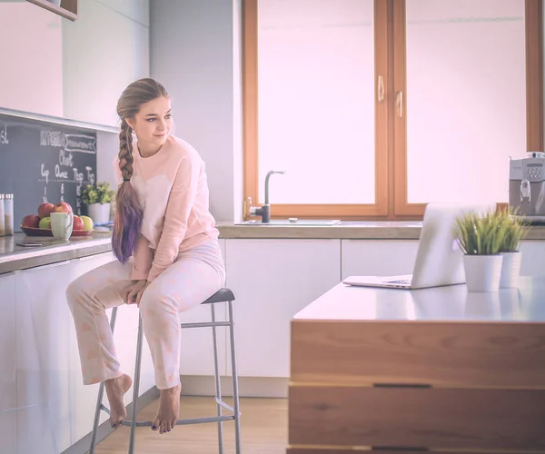 Jovem mulher sentada na mesa na cozinha . — Fotografia de Stock