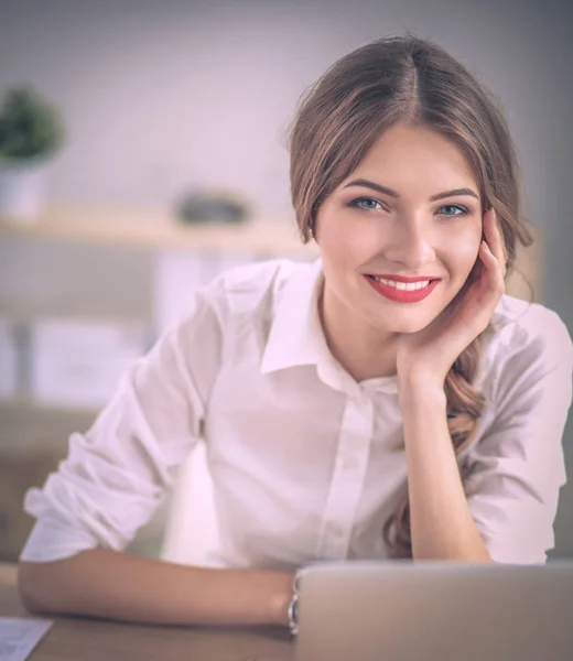 Attraktiv affärskvinna sitter på ett skrivbord med bärbar dator på kontoret — Stockfoto