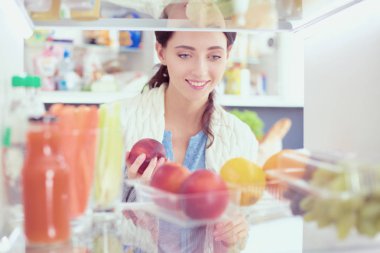 Sağlıklı yiyecek, sebze ve meyvelerle dolu açık buzdolabının yanında duran kadın portresi. Kadın portresi