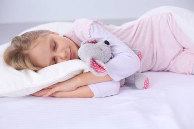 çocuk oyuncak oyuncak ayı ile yatakta uyur küçük kız.