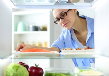 Sağlıklı yiyecek, sebze ve meyvelerle dolu açık buzdolabının yanında duran kadın portresi..