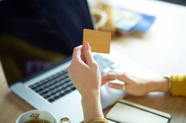 Kredi kartı tutan ve dizüstü bilgisayar kullanan genç bir kadın. Çevrimiçi alışveriş kavramı
