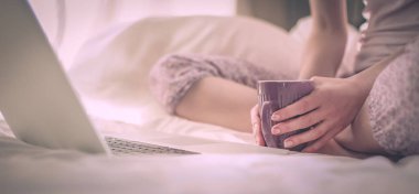 Dizüstü bilgisayar ile yatakta oturan genç güzel kadın