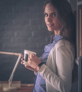 Portre rahat genç bir kadın masasında oturmuş elinde bir fincan kahve tutuyor.