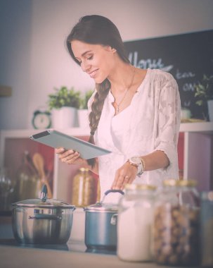 Mutfakta yemek yapmak için tablet bilgisayar kullanan genç bir kadın.