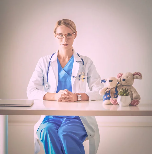 Mooie jonge glimlachende vrouwelijke arts zittend aan het bureau. — Stockfoto