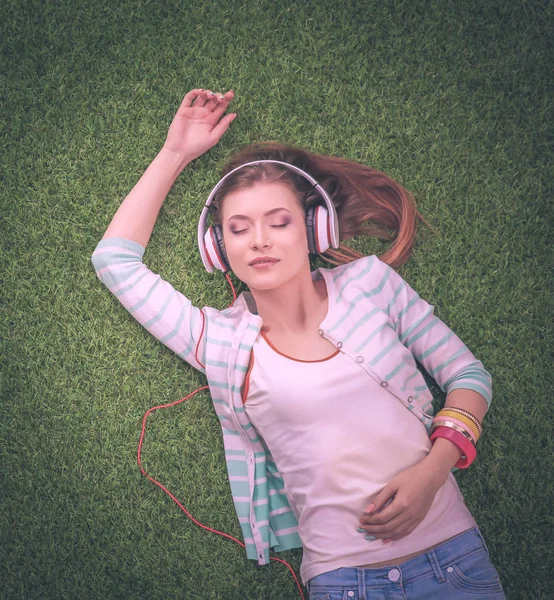 Jonge vrouw luisteren naar de muziek, liggend op groen gras — Stockfoto