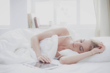 Elinde boş ekranlı dijital tablet tutan ve yatak odasında kameraya gülümseyen bir kız.