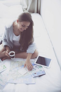 Bir fincan kahve ve dijital tabletle yatakta oturan rahat genç bir kadın.