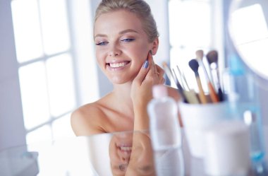 Bornozlu genç kadın banyo aynasına bakıyor.