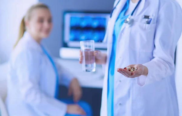 Colpo di dottore che tiene pillole e vetro d'acqua a clinica con collega sullo sfondo. — Foto Stock