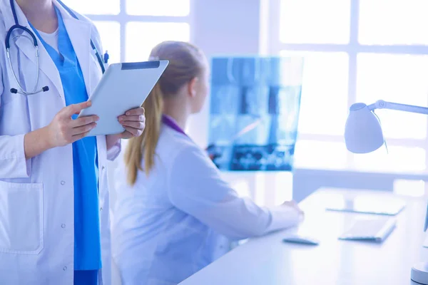 Close up shoot of doctors hands holding tablet and colleague sitting at the table on the background. — Stock Photo, Image