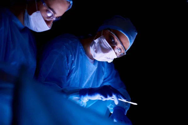 Equipo de médicos en cirugía en un fondo oscuro. — Foto de Stock