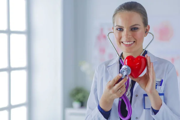 Un médecin avec stéthoscope examinant le cœur rouge, isolé sur fond blanc — Photo