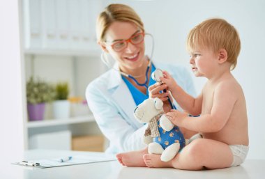 Kadın doktor, klinikte steteskoplu bir çocuğu dinliyor.