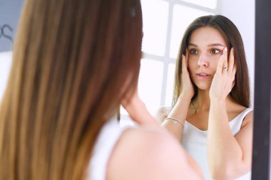 Genç kadın kendini evde aynada yansıma arıyor.