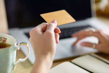 Kredi kartı tutan ve dizüstü bilgisayar kullanan genç bir kadın. Çevrimiçi alışveriş kavramı