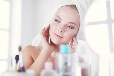 Bornozlu genç kadın banyo aynasına bakıyor.