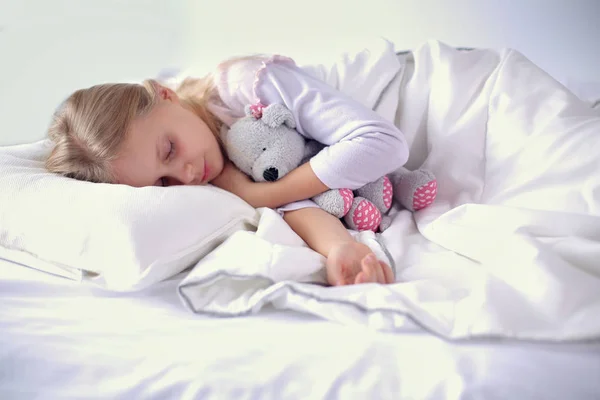 Niño niña duerme en la cama con un osito de peluche de juguete . — Foto de Stock