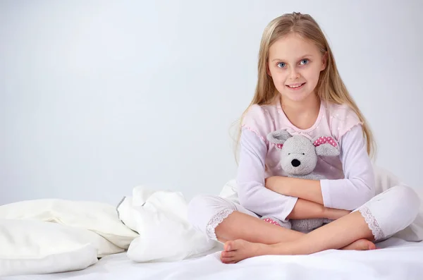 La niña en el dormitorio está sentada en la cama. La niña está usando un pijama y sentada en la cama  . —  Fotos de Stock