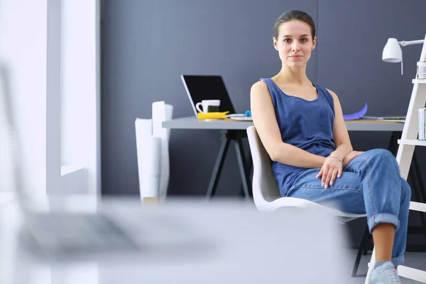 Mladá žena sedí za stolem s nástroji, plánem a notebookem. — Stock fotografie
