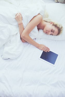 Elinde boş ekranlı dijital tablet tutan ve yatak odasında kameraya gülümseyen bir kız.