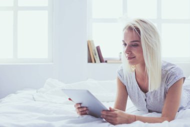 Elinde boş ekranlı dijital tablet tutan ve yatak odasında kameraya gülümseyen bir kız.