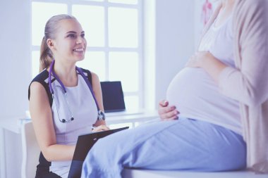 Steteskoplu ve tabletli genç kadın doktor hastanede hamile bir kadınla konuşuyor..
