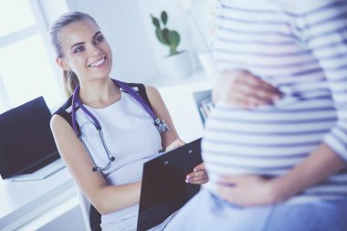 Steteskoplu ve tabletli genç kadın doktor hastanede hamile bir kadınla konuşuyor..