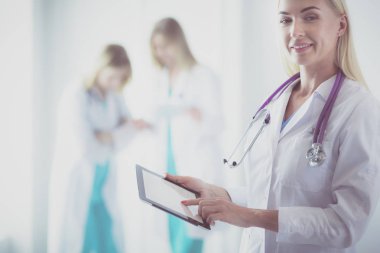 Genç bir kadın doktorun portresi, elinde aipad ile, bir tıp ofisinde.