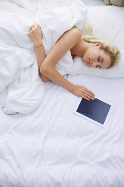 Elinde boş ekranlı dijital tablet tutan ve yatak odasında kameraya gülümseyen bir kız.