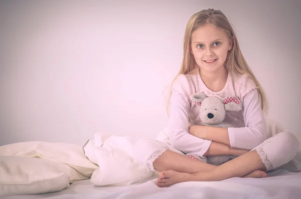Das kleine Mädchen im Schlafzimmer sitzt auf dem Bett. kleines Mädchen trägt Schlafanzug und sitzt im Bett . — Stockfoto