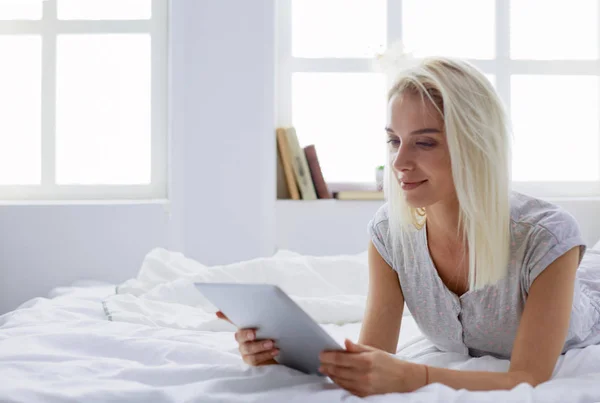 Menina segurando tablet digital com tela em branco e sorrindo para a câmera no quarto — Fotografia de Stock