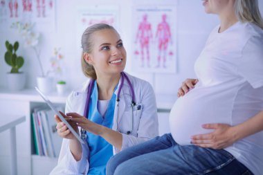 Gülümseyen kadın doktor resimlerini tablette hastanedeki hamile genç bayana gösteriyor..