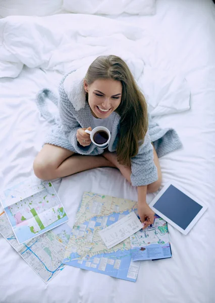 Jeune femme détendue assise sur le lit avec une tasse de café et une tablette numérique — Photo