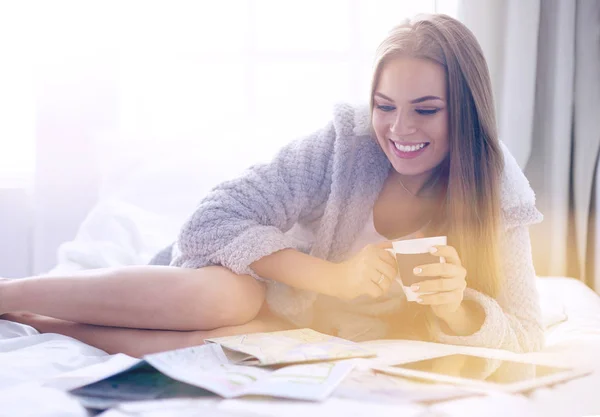 Mujer joven y relajada sentada en la cama con una taza de café y una tableta digital — Foto de Stock