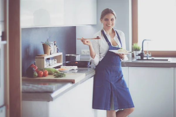 Jovem mulher em pé junto ao fogão na cozinha — Fotografia de Stock