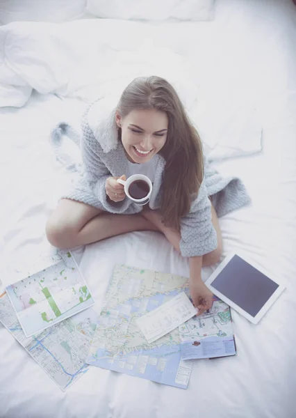 Mujer joven y relajada sentada en la cama con una taza de café y una tableta digital —  Fotos de Stock