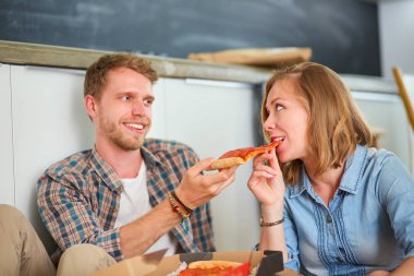 Genç çift, yeni bir eve taşındıktan sonra etraflarında kutularla yerde pizza molası veriyorlar. Genç çift