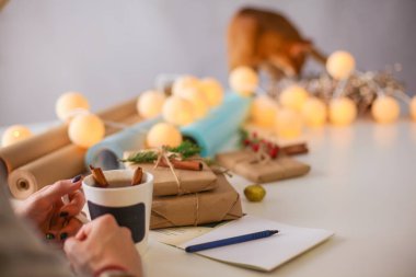 Noel hediye kutusu ile masaya oturan kadın. Kadının elleri