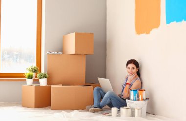 Yeni daire dizüstü bilgisayar ile oturup, boyama sırasında genç kadın portre. Dizüstü bilgisayar ile genç kadın