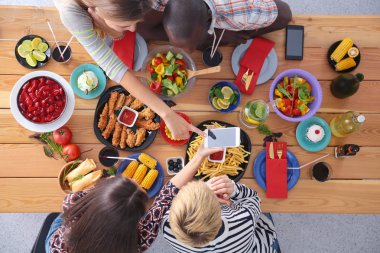 Ahşap masada otururken birlikte yemek yiyen bir grup insanın üst düzey görüntüsü. Masada yemek var. İnsanlar fast food yiyor..
